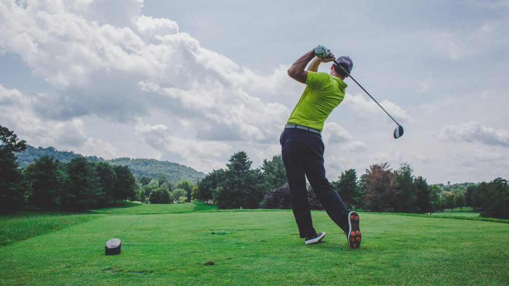 A man swinging at a golf ball on the green.