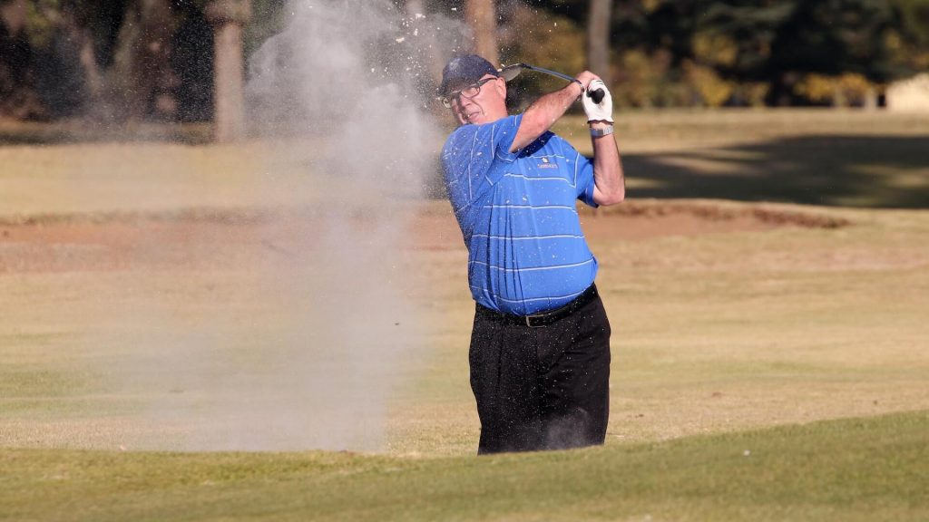 A man swinging at a golf ball with his club.