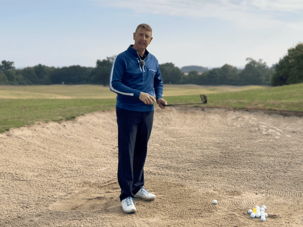 A man standing on top of a sandy hill holding a golf club.