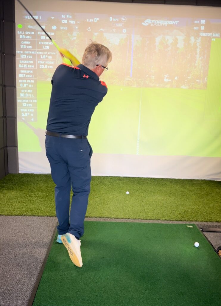 Man swinging golf club in simulator.