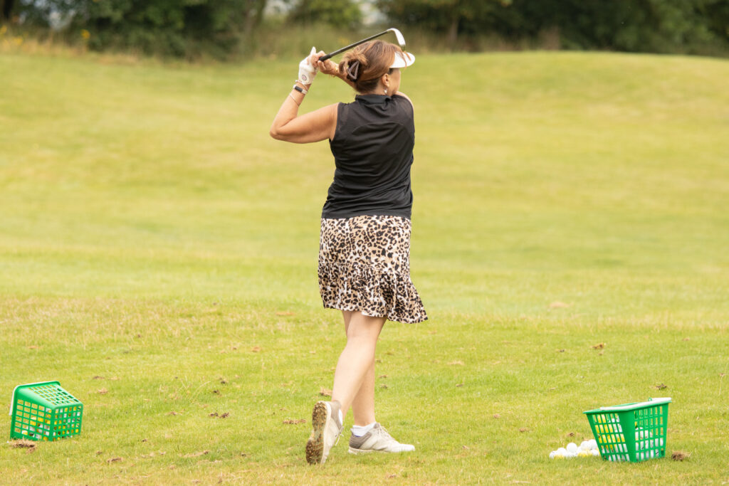 Woman in leopard skirt golfing on green.