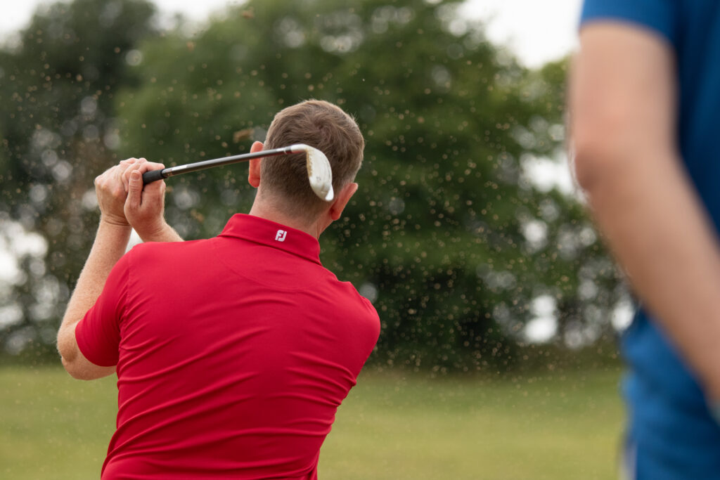 Golfer swings a golf club on a course.