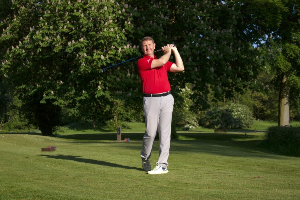 Man in red shirt golfing on green.